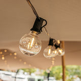 G40 globe LED replacement bulbs glowing warm white on black string lights strung beneath an outdoor tent ceiling