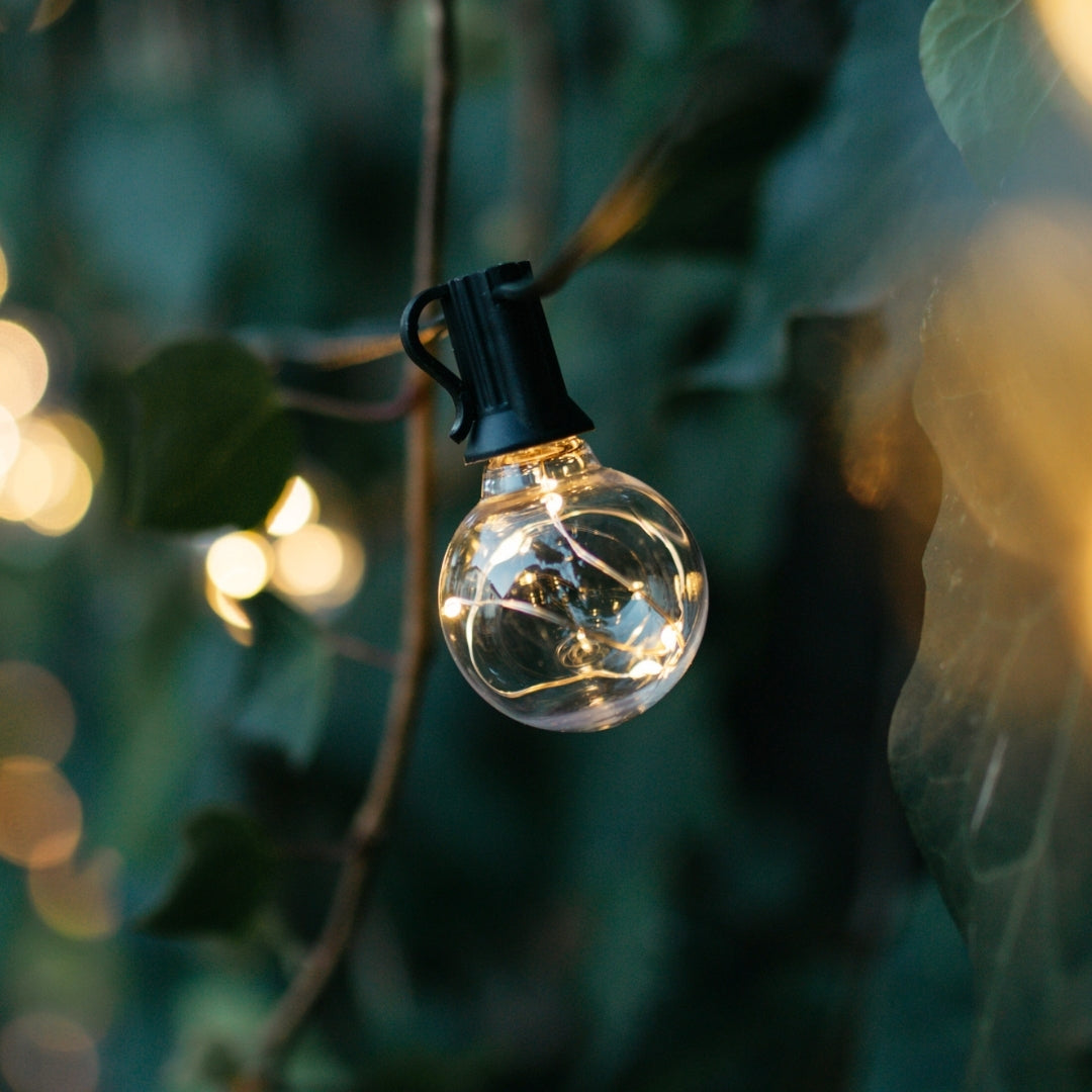 G40 wire LED replacement bulb with copper wire detail hanging outdoors among green foliage at dusk