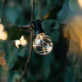 G40 wire LED replacement bulb with copper wire detail hanging outdoors among green foliage at dusk