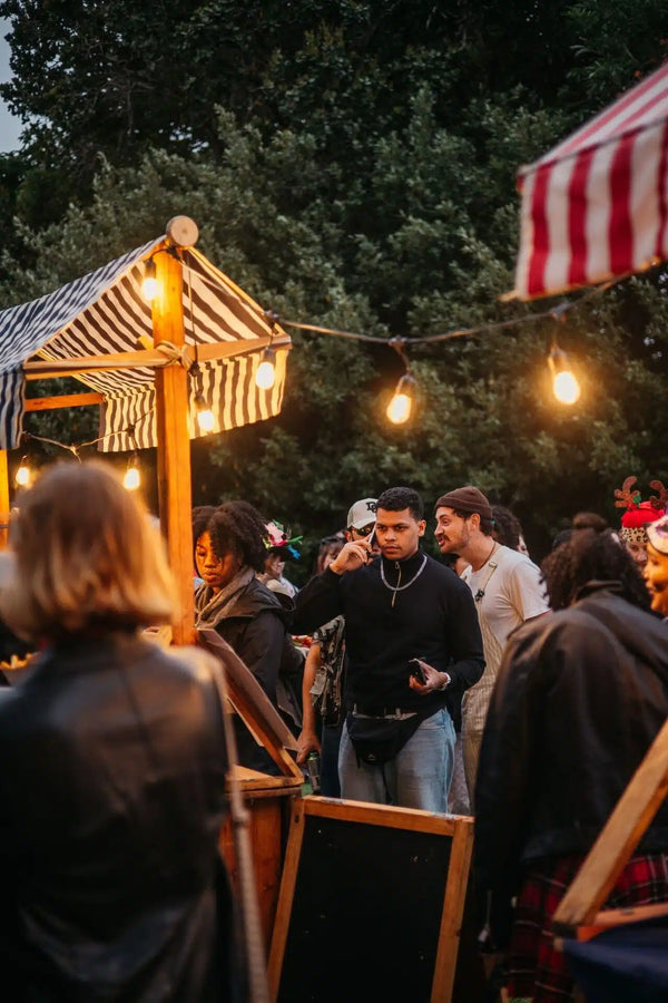 Outdoor gathering with people around a wooden structure under string lights.
