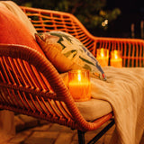 Wicker chair with a flameless glass candle and decorative pillow on a blurred outdoor background