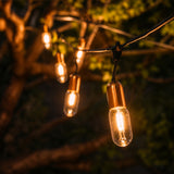 Gold Drop String Lights with warm golden T45 tubular bulbs suspended on individual drop wires on black cable creating a dramatic pendant effect in a styled South African outdoor space at dusk