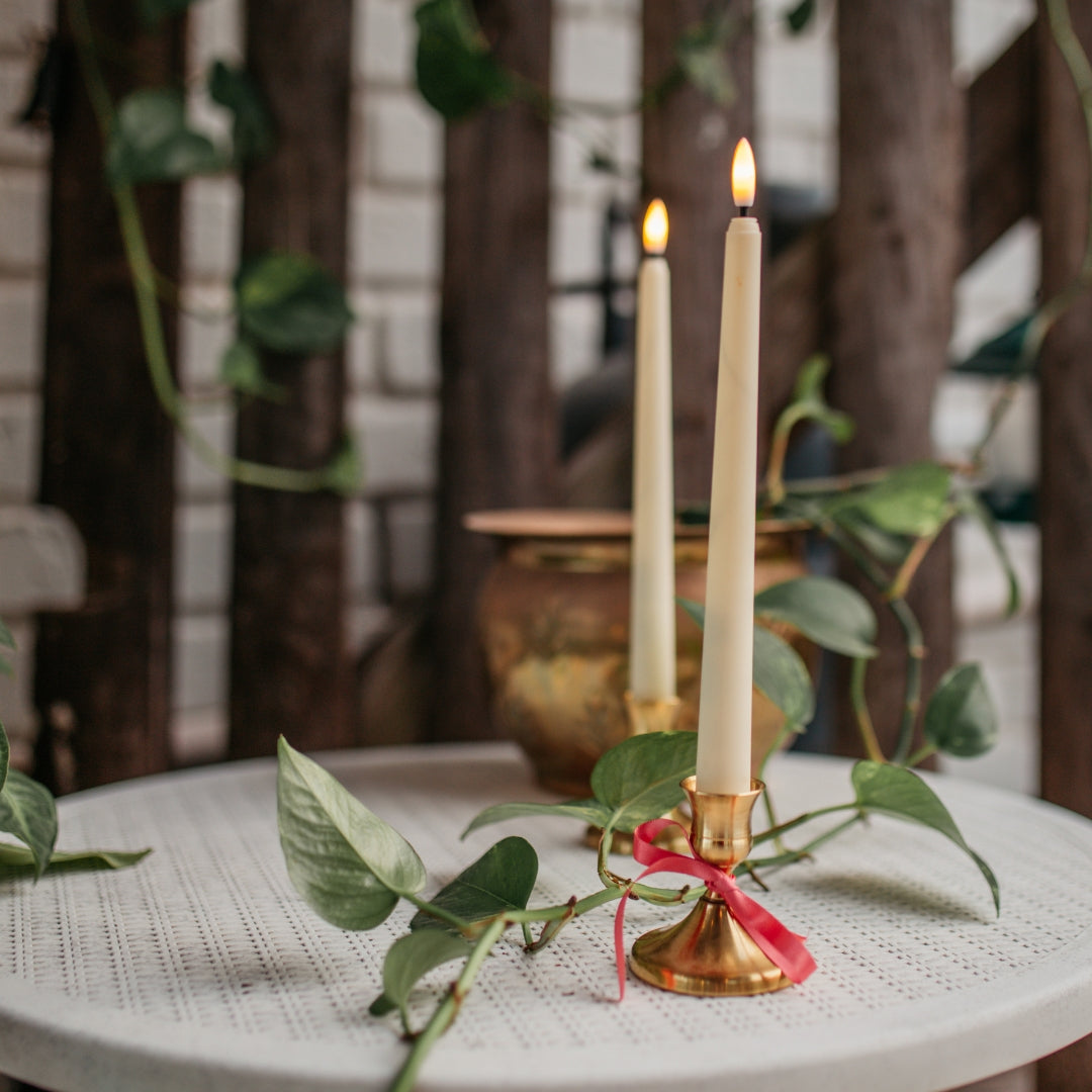 Decorative candles on a table with greenery and a blurred indoor background