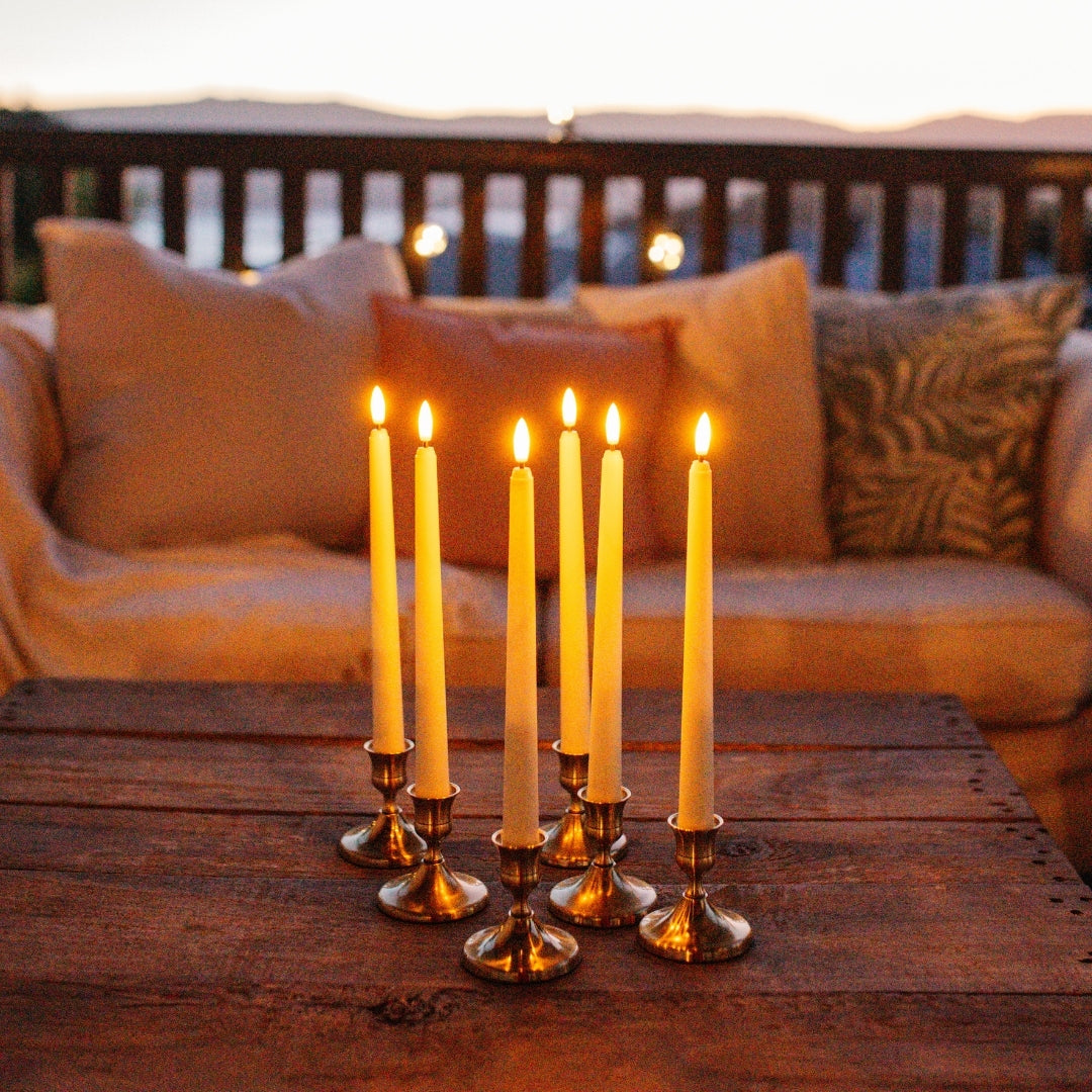 Six ivory flameless taper candles glowing in brass candlestick holders creating warm ambient atmosphere