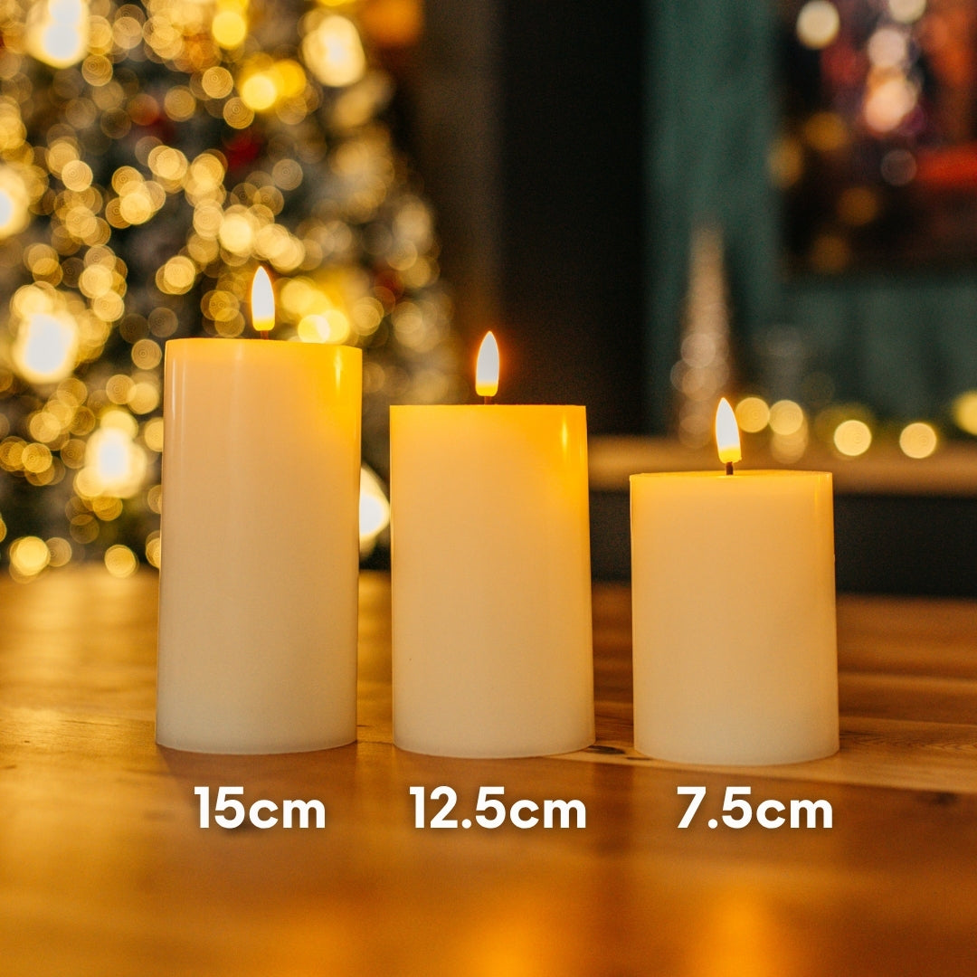 Set of three ivory real wax flameless LED pillar candles on a wooden table showing graduated heights of 15cm, 12.5cm, and 10cm with Christmas bokeh background