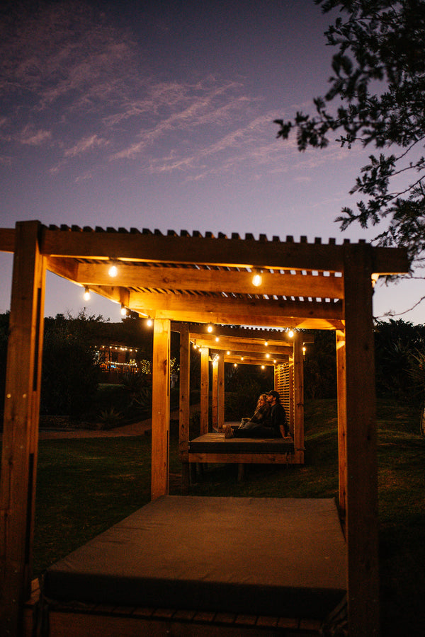 Wooden pergola with solar string lights at night, couple sitting underneath