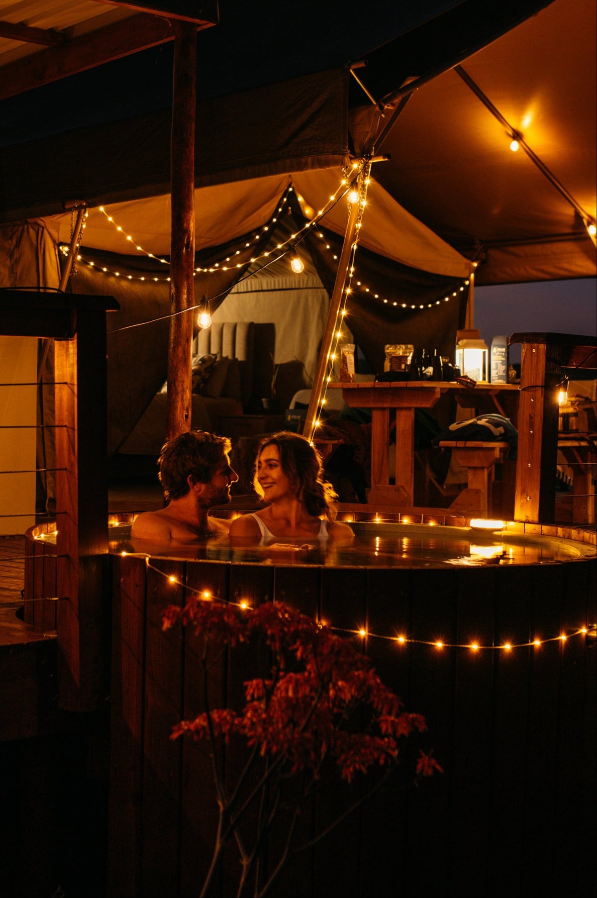 Two people in a hot tub under string lights at night.