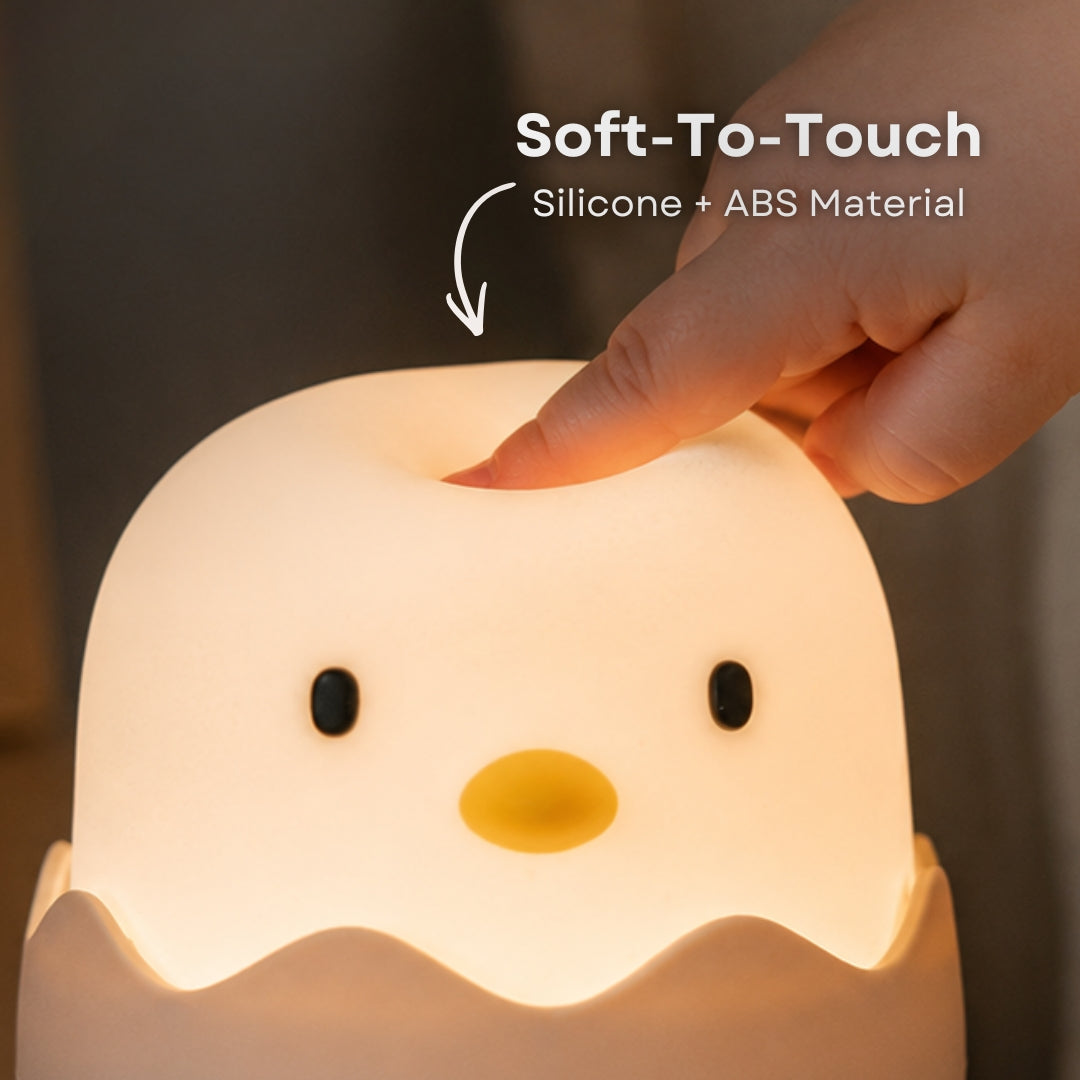 Hand touching the soft silicone surface of the Lightie Egg night light glowing warm white with soft to touch and silicone plus ABS material callout