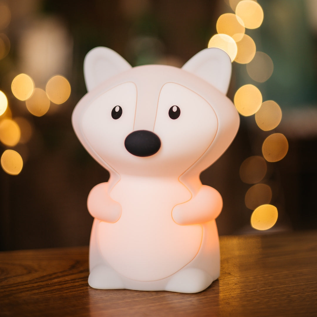 Lightie Fox silicone kids night light glowing warm white on a wooden surface with warm golden bokeh fairy lights in the background