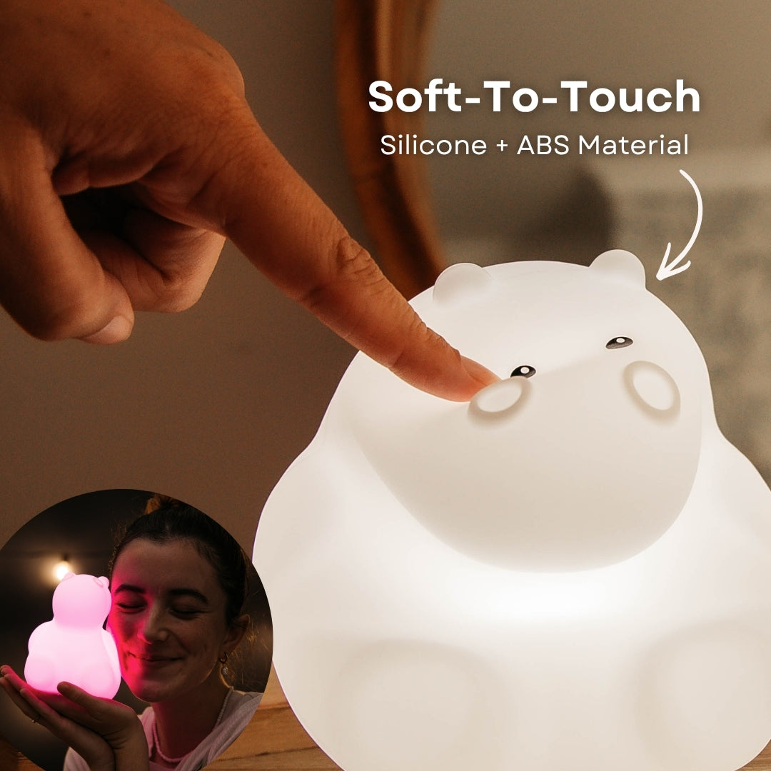 Finger pressing into the soft silicone surface of the Lightie Hippo night light glowing warm white with soft to touch and silicone plus ABS material callout