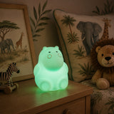 Lightie Hippo silicone kids night light glowing warm white on a wooden surface with warm golden bokeh fairy lights in the background
