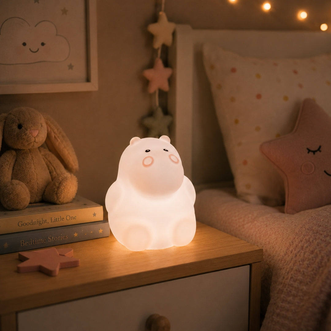Lightie Fox silicone kids night light glowing warm white on a wooden bedside surface with cushions in the background