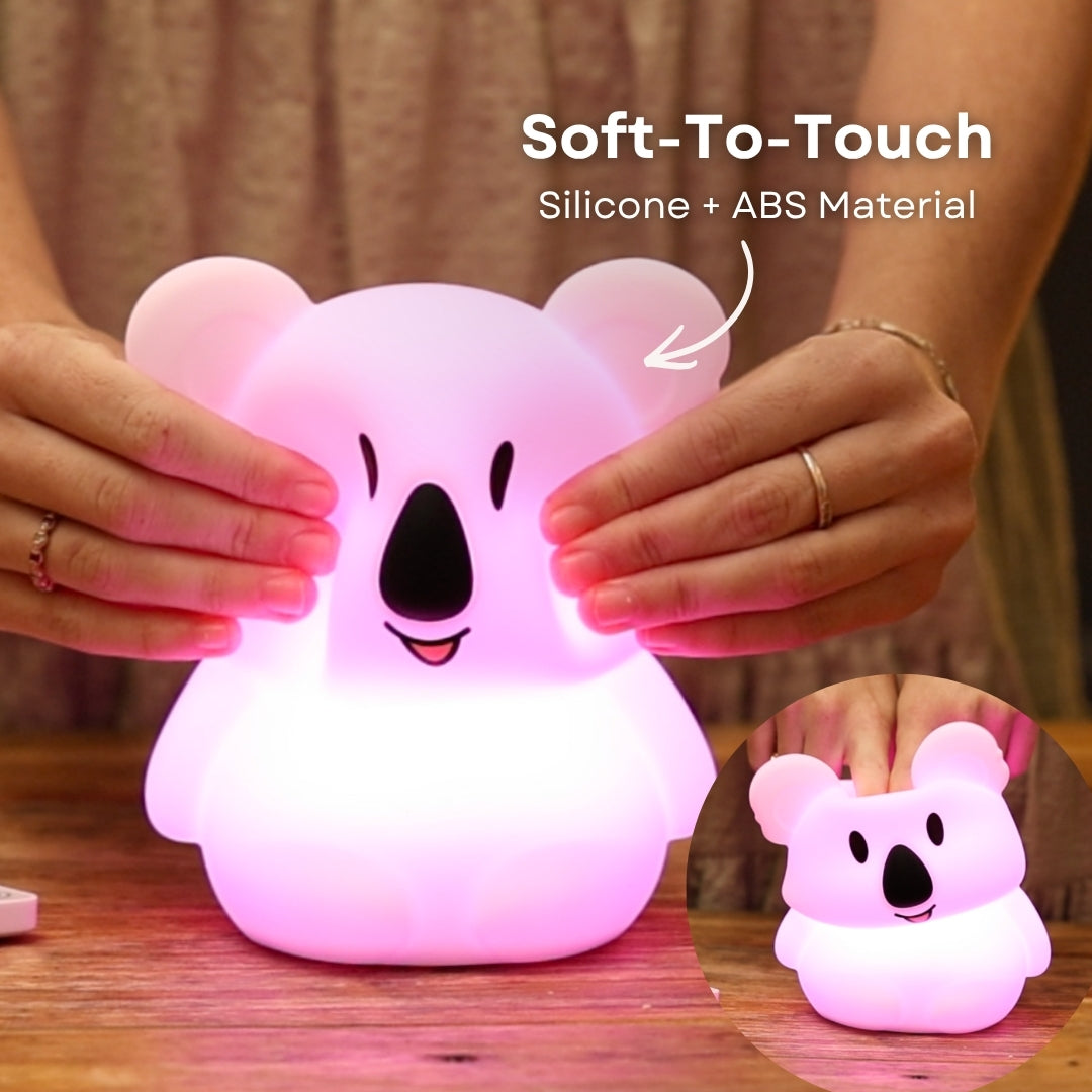 Finger pressing into the soft silicone surface of the Lightie Koala night light glowing warm white with soft to touch and silicone plus ABS material callout