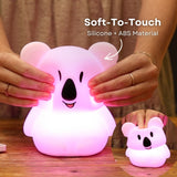 Finger pressing into the soft silicone surface of the Lightie Koala night light glowing warm white with soft to touch and silicone plus ABS material callout