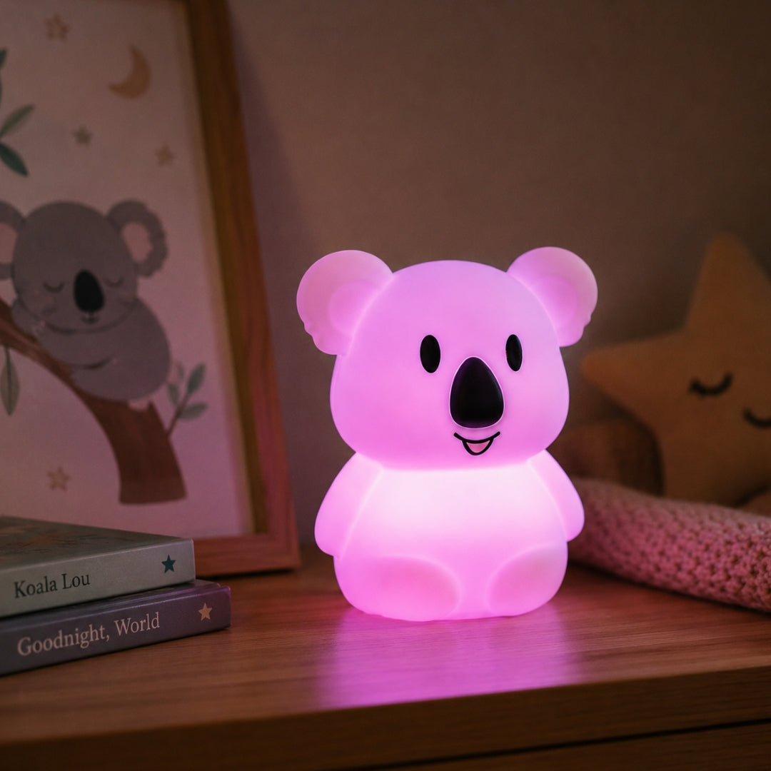 Lightie Koala silicone kids night light glowing warm white on a wooden bedside surface with cushions in the background