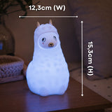 Hands holding the Lightie Llama night light glowing pink with dimension callouts showing 12.3cm width and 15.3cm height