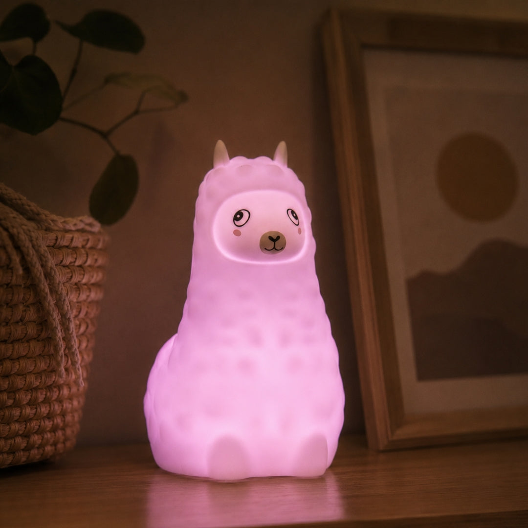 Lightie Llama silicone kids night light glowing teal on a bedside table in a softly lit children's room with fairy lights in the background