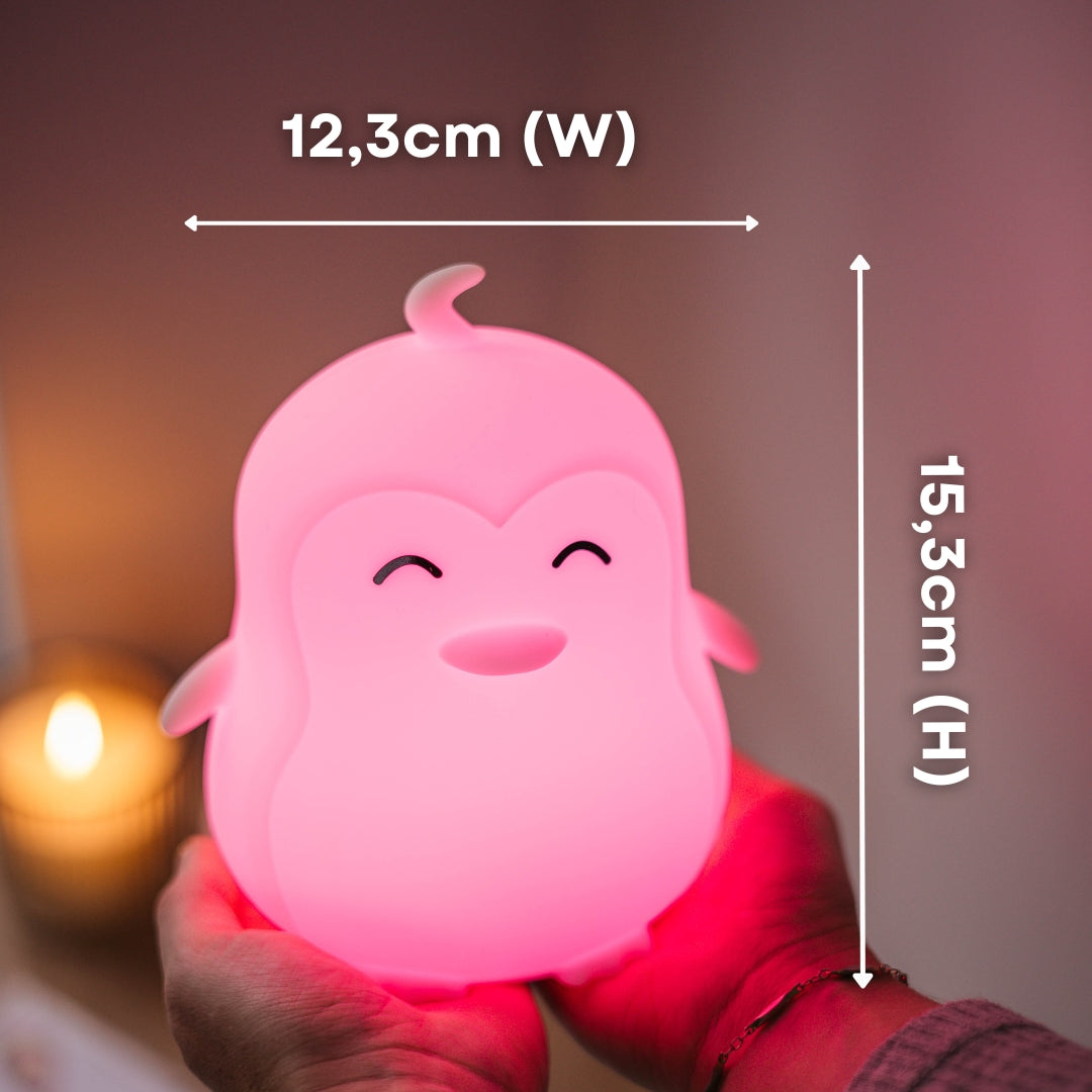 Hands holding the Lightie Penguin night light glowing pink with dimension callouts showing 12.3cm width and 15.3cm height