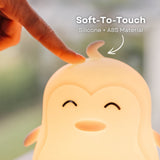 Finger pressing into the soft silicone surface of the Lightie Penguin night light glowing warm white with soft to touch and silicone plus ABS material callout