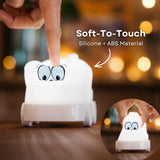 Hand touching the soft silicone surface of the Lightie Truck night light glowing warm white with soft to touch and silicone plus ABS material callout