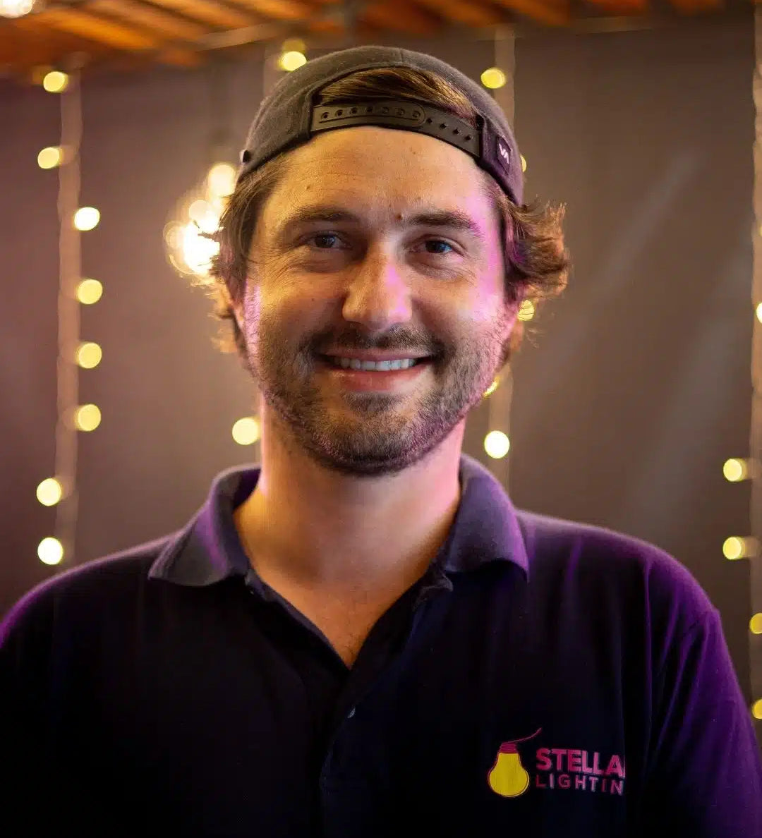 Man wearing a blue shirt with a Stellar Lighting logo, standing in front of string lights.