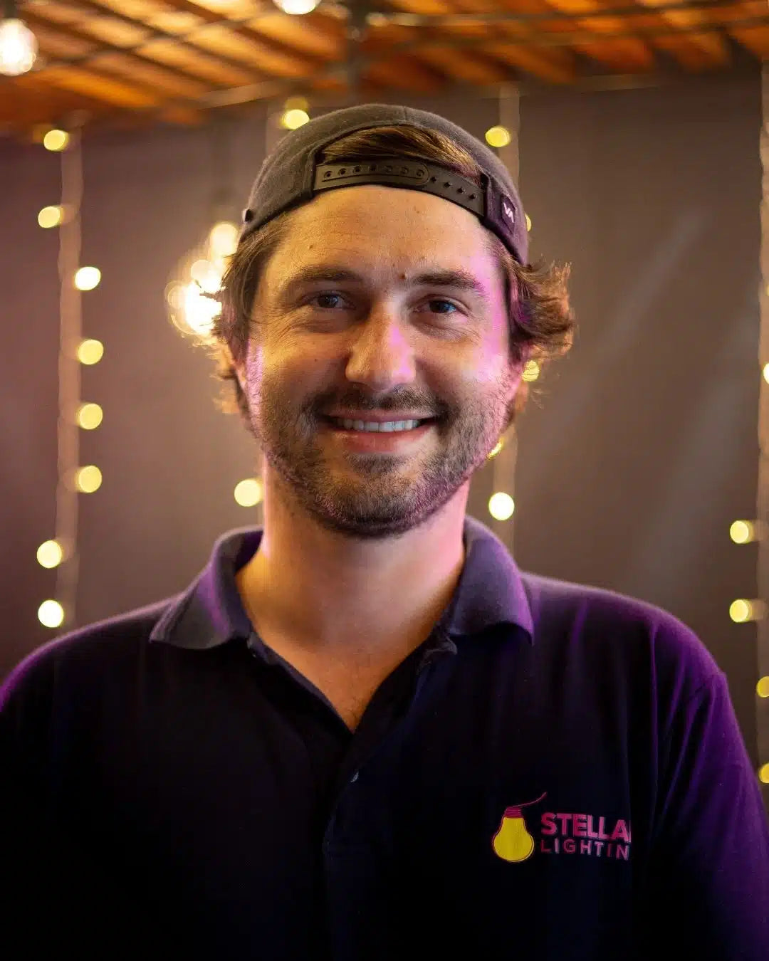 Man wearing a blue shirt with a Stellar Lighting logo, standing in front of string lights.