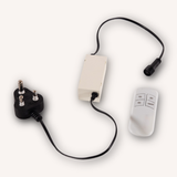 A white electronic control box with a black power cord featuring a SA three-pin plug and a black cable ending in a connector, alongside a white remote control with buttons, all on a light off-white background.