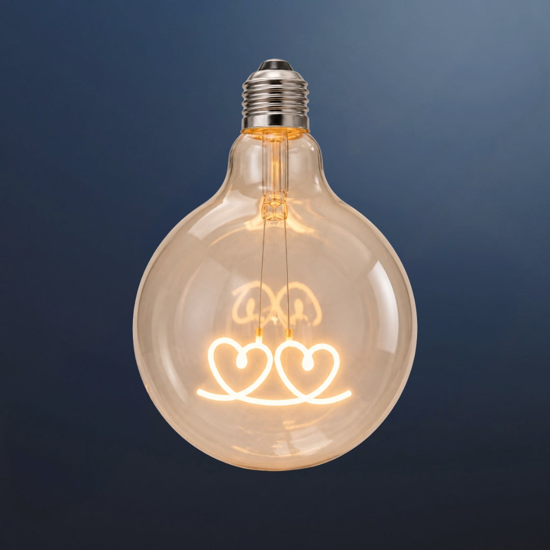 Single G125 globe LED bulb with two heart shaped filament detail and clear glass on a dark navy background