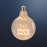 Single G125 globe LED bulb with two heart shaped filament detail and clear glass on a dark navy background