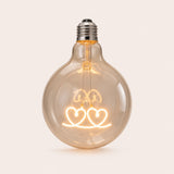 Single G125 globe LED bulb with two heart shaped filament detail and clear glass on a light background