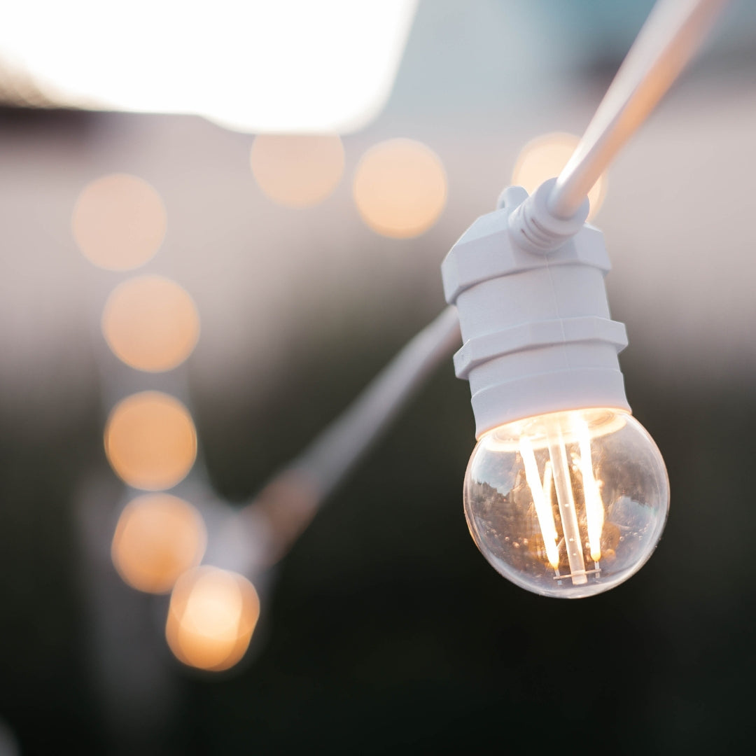 Close-up of warm white G45 retro globe bulb on heavy duty white festoon string lights cable against a soft outdoor background