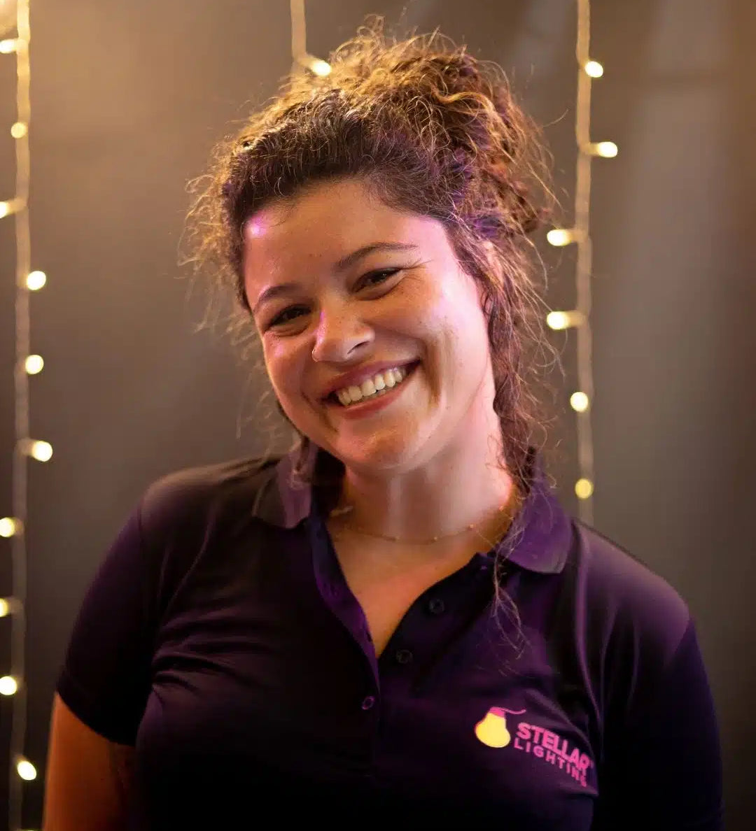 Woman wearing a dark polo shirt with a Stellar Lighting logo against a string of lights background