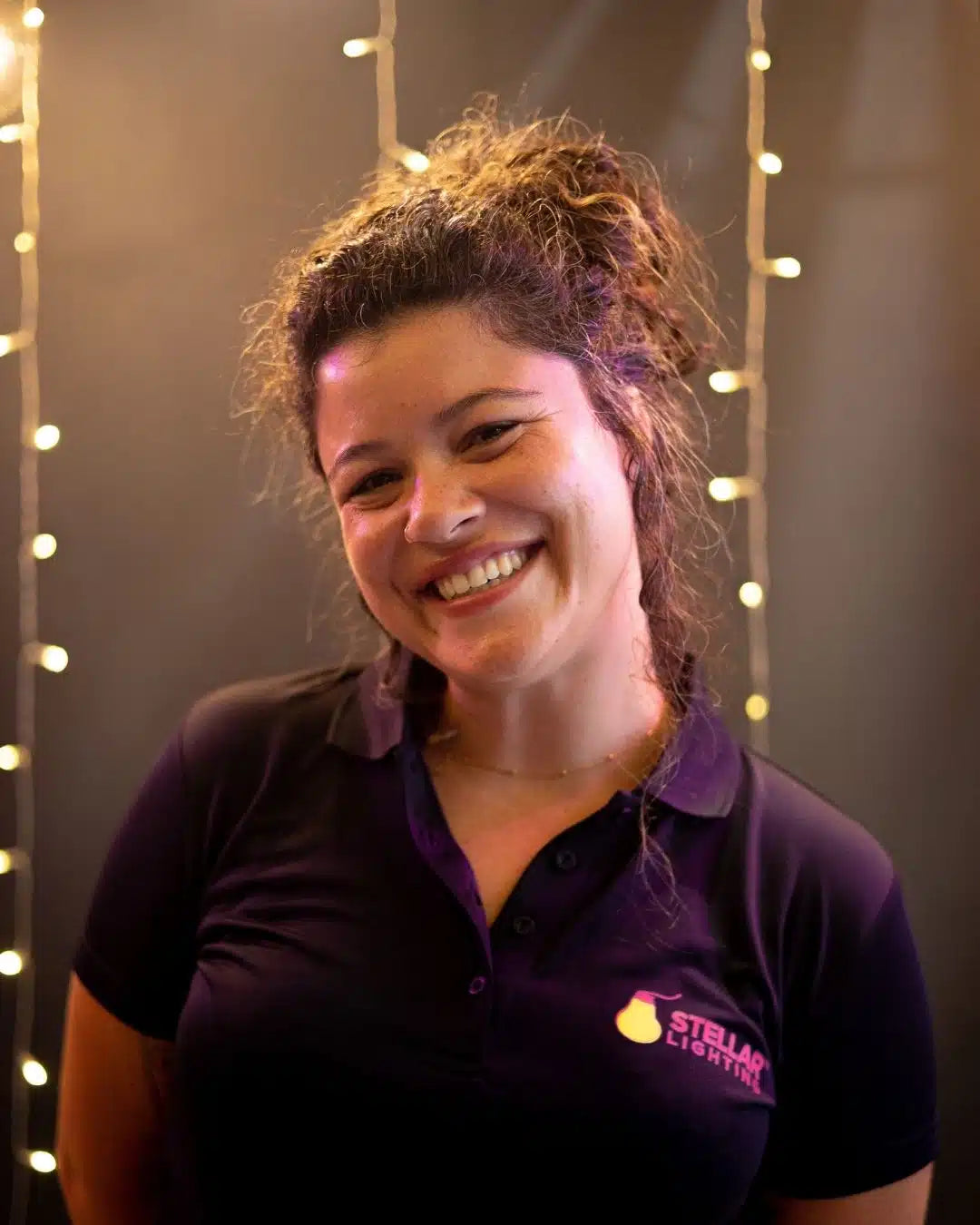 Woman wearing a dark polo shirt with a Stellar Lighting logo against a string of lights background