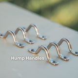 Four silver metal hump handles arranged on a light beige surface with a blurred green outdoor background. The text 'Hump Handles' is overlaid near the bottom.