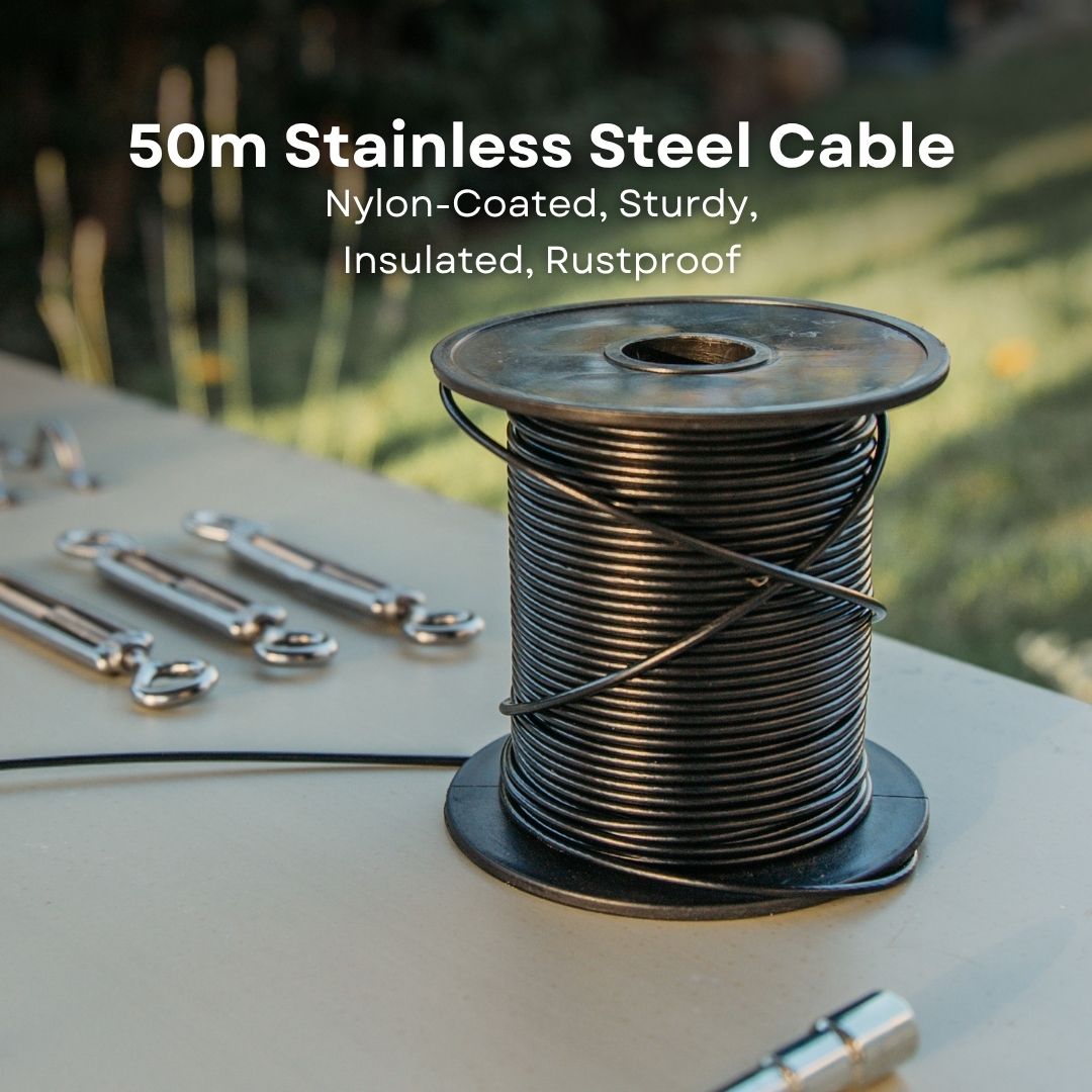 A spool of 50m stainless steel cable with a black nylon-coated wire, displayed on a beige table outdoors with metal hardware and a blurred green garden background. White text at the top reads '50m Stainless Steel Cable Nylon-Coated, Sturdy, Insulated, Rustproof'.