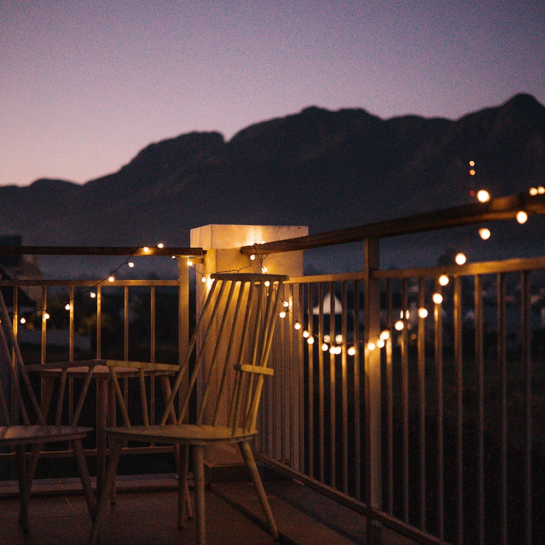 Balcony with fairy lights and chairs at night with mountains in the background