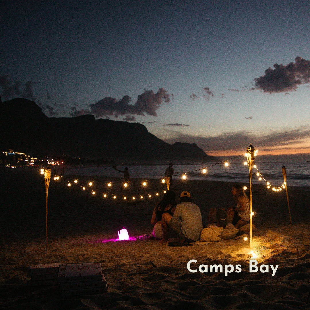 Solar Classic String Lights with warm white G40 globe bulbs strung in a beach evening setup at Camps Bay alongside tiki torches creating a warm festive atmosphere