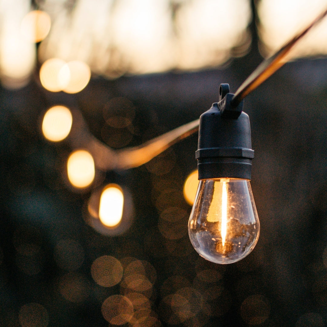 Close-up of warm white S14 vintage LED bulb on black IP66 weatherproof solar festoon string lights against a soft outdoor background