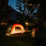 Solar string lights glowing around a camping tent with camp chairs in a dark garden at night
