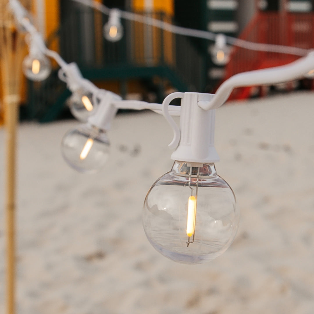 Close-up of G40 globe LED bulb on white cable glowing with warm white light at a beach location