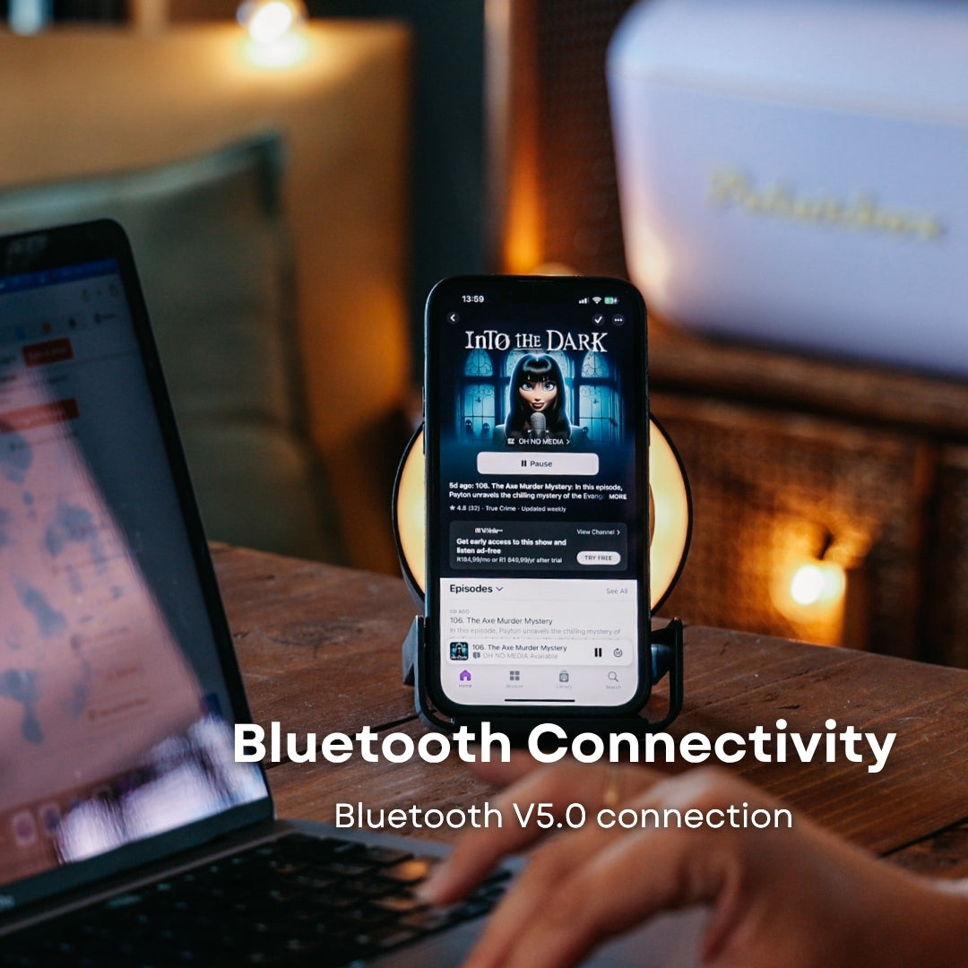 Smartphone on black speaker wireless charger streaming audio with laptop open in the background and Bluetooth V5.0 callout