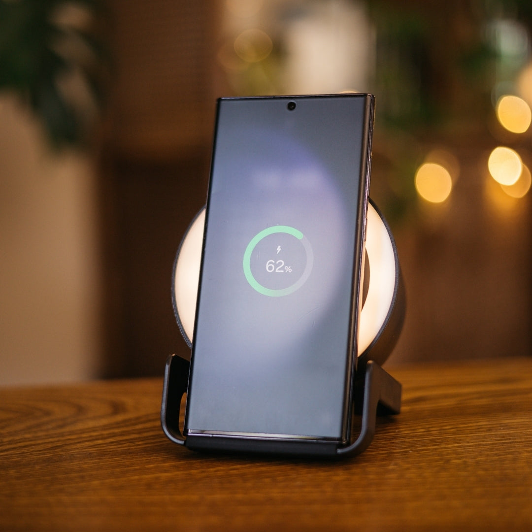 Smartphone resting on black speaker wireless charger displaying 62 percent wireless charging indicator with warm bokeh background