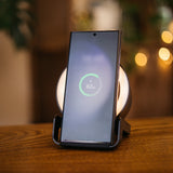 Smartphone resting on black speaker wireless charger displaying 62 percent wireless charging indicator with warm bokeh background