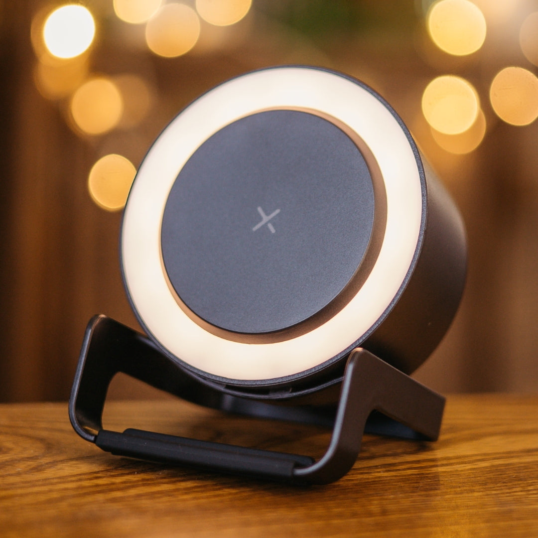 Black speaker wireless charger with glowing LED ring light on a wooden surface with warm bokeh in the background