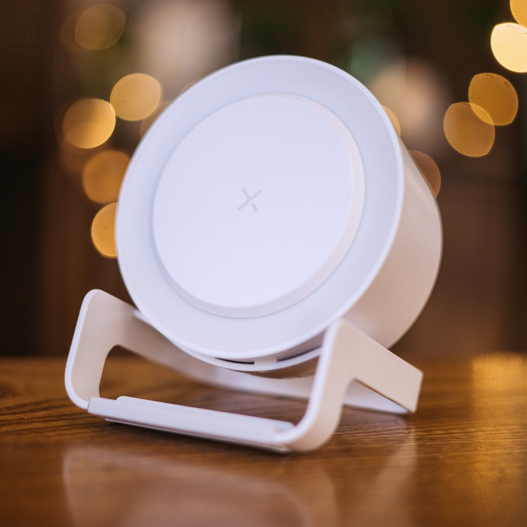 White speaker wireless charger with glowing LED ring light on a wooden surface with warm bokeh in the background