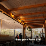 Ultimate Festoon String Lights strung along wooden ceiling beams at Peregrine Farm Stall outdoor terrace with customers seated below at dusk