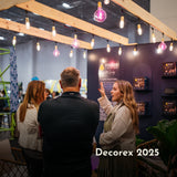 People talking under the Ultimate Gold Drop String Lights with warm golden T45 tubular bulbs on individual drop wires creating a dramatic warm amber glow at Decorex Cape Town in South Africa