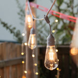 Close-up of warm white ST64 LED bulb suspended on individual drop wire on white IP66 weatherproof drop string lights against an outdoor background