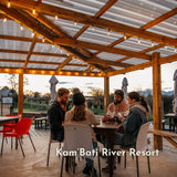 Group of friends gathered under vintage string lights on a covered pergola at Kam'Bati River Resort at sunset