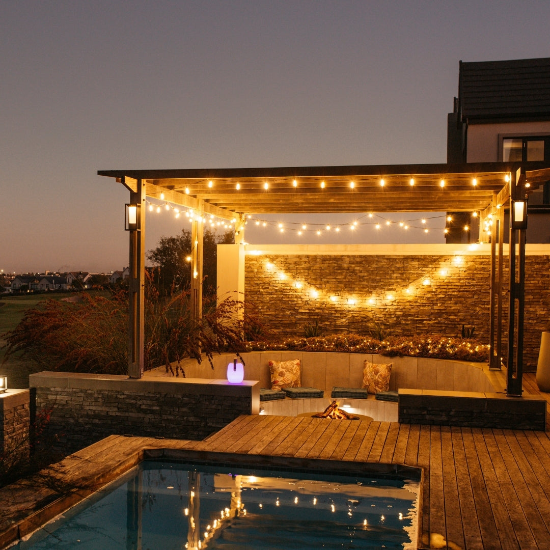 Vintage string lights strung across a pergola over a pool and deck at night creating warm amber atmosphere